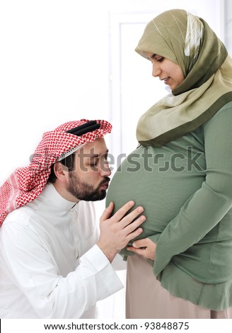 Pregnant muslim wife smiling with her husband kissing belly,and his hands on belly