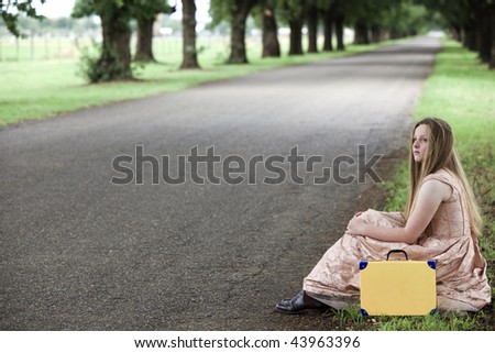 Pretty girl sitting by road with suitcase