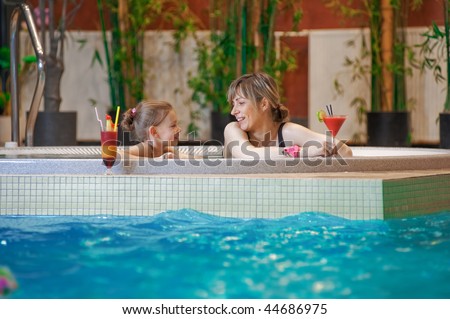 Happy mother and daughter relaxing by the pool with glass of coctail