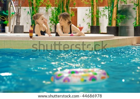 Happy mother and daughter relaxing by the pool with glass of coctail