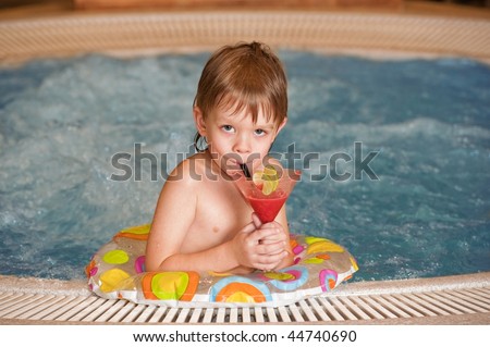 Happy little boy relaxing by the pool with glass of coctail