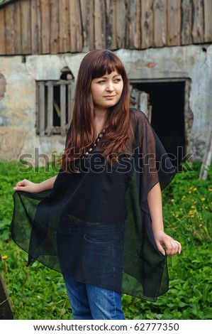 Young beautiful woman stand in the garden nearby old cattle-shed.