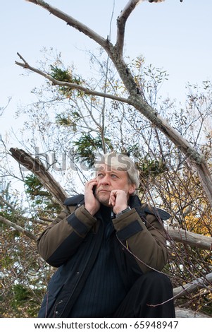 Mature busy man with grey hair in forest talking on the phone in autumn day.