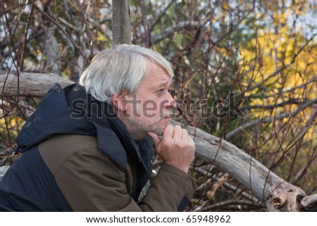 Portrait of mature thoughtful man with grey hair in forest in autumn day.