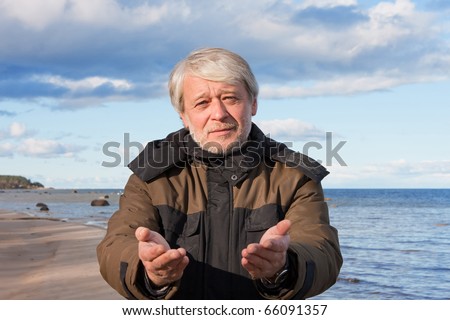 Mature poor man with grey hair at the Baltic sea asks for help in autumn day.