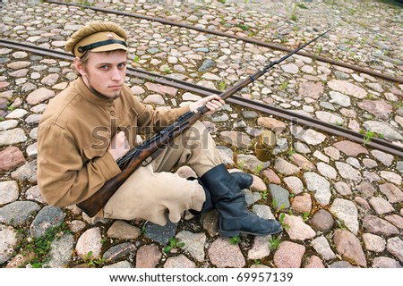 Soldier with gun and boiler in uniform of World War I, sit down and resting on the pavement. Costume accord the times of World War I. Photo made at cinema city Cinevilla in Latvia.