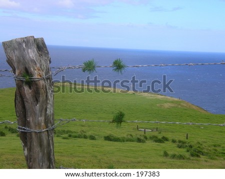 cross overlooking ocean threw a wire fence with old fence post