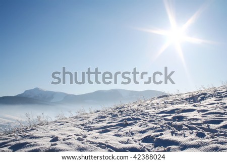 Horizontal snow covered mountains under blue sky and shiny sun