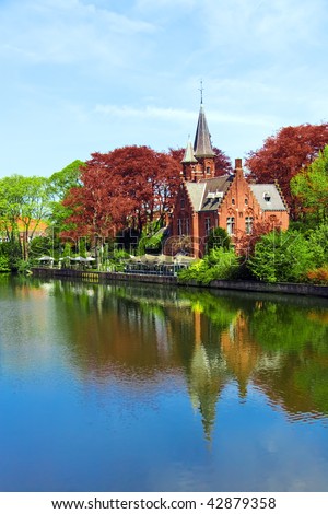 Old red brick castle and green trees reflected in water under blue sky