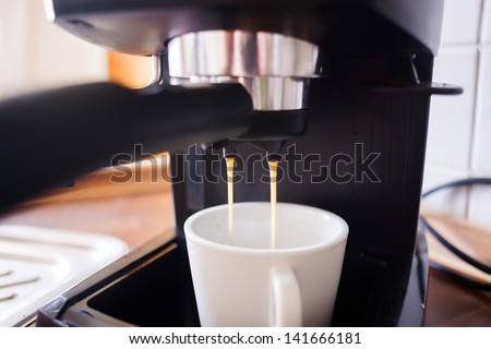 Close-up on coffee maker pouring hot espresso into a cup.