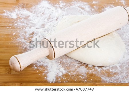 Dough with rolling pin on wooden board.