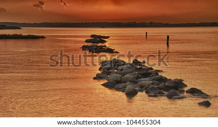 Sun about to set on the Indian River in Delaware with rocks and night heron in foreground