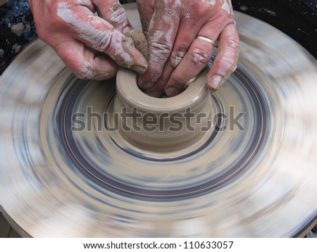 Potter spinning and shaping wet clay in the shape of a cup