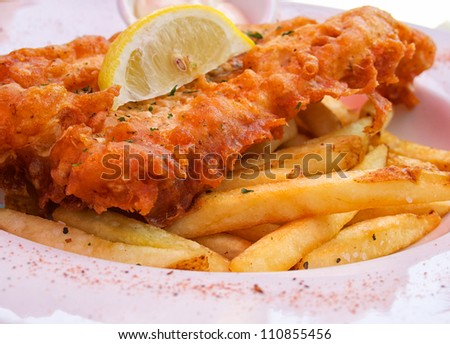 Closeup of flash fried fish and chips on plate with lemon slice