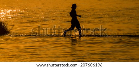 Silhouette of a youth running in the shallow waters of the Indian River Inlet (Delaware).