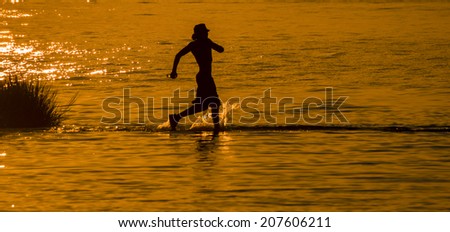 Silhouette of a youth running in the shallow waters of the Indian River Inlet (Delaware).