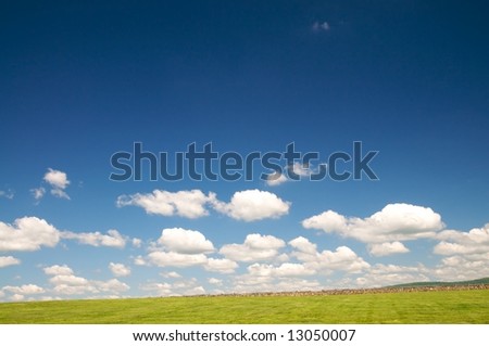 Horizontal photo of sweeping landscape of pasture and old fence against blue sky and clouds