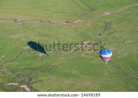 Horizontal photo with shadow of hot air balloon and its basket cast on ground below and actual balloon on right