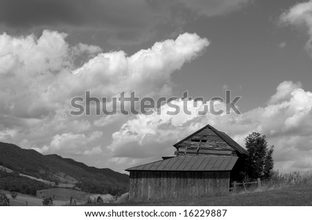 Horizontal black and white photo of large wooden barn against dramatic sky and Blue Ridge mountains of Virginia
