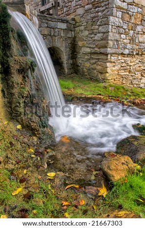 Vertical photo of old stone mill with mill race waterfall in foreground