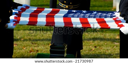 Horizontal photo of US flag held over funeral urn at burial ceremony at Arlington National Cemetery