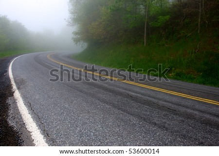 Two lane highway disappearing around curve into early morning fog