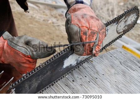 Man wearing leather gloves sharpening chainsaw with file.