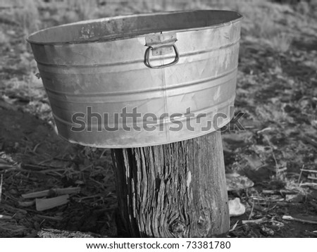 Old galvanized metal wash tub sitting outside on tree stump, black and white image. Remote Catron County, New Mexico, USA.