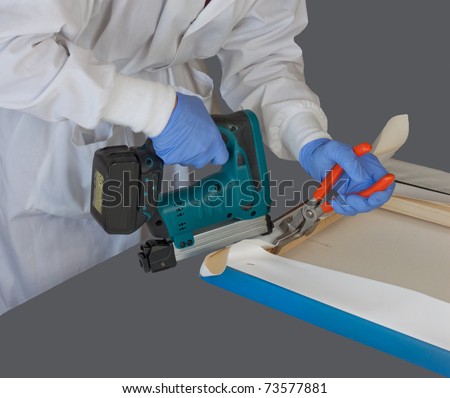 Woman wearing a white lab coat and protective nitrile gloves while stretching canvas fine art photograph print using canvas stretcher pliers and staple gun.