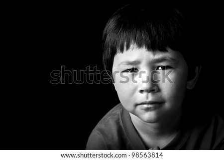 Cute young asian boy with serious look on black background in black and white