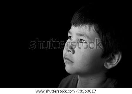 Cute young asian boy looking up with serious look on black background in black and white
