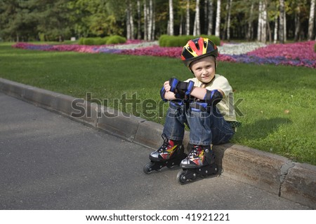 The tired boy on the roller blades and in a protective helmet sits on a border.