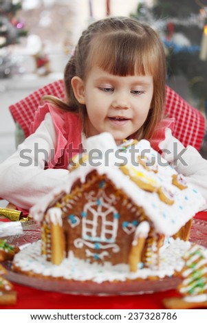 Little beautiful girl with a house of gingerbread dough