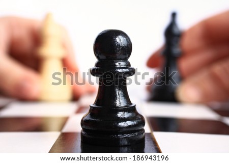 Two human hands move the chess pieces on a chess piece pawn background closeup.