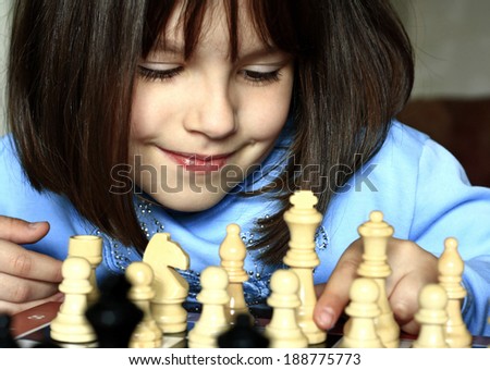 Little girl learning to play chess in the room.