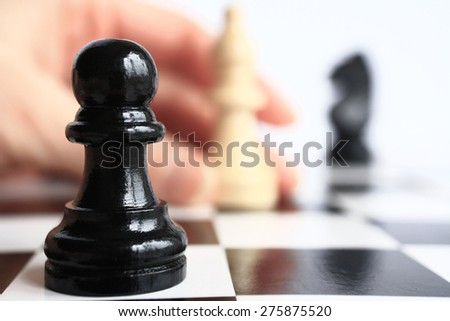 Human hand moves a chess piece on a chess board on a background of a pawn chess piece closeup.