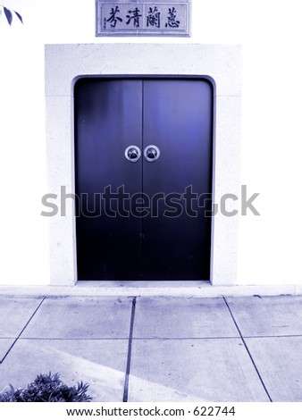 Chinese Temple door in dark blue tones stands out on white stucco wall.