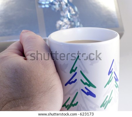 Hand holds Christmas mug with coffee in front of silver metallic wrapped gift package.