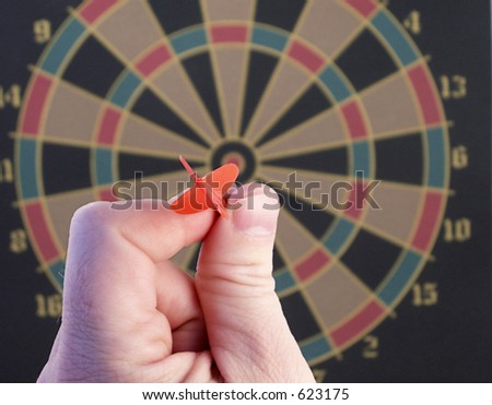 Focus on hand and dart as bullseye and empty board loom in background.