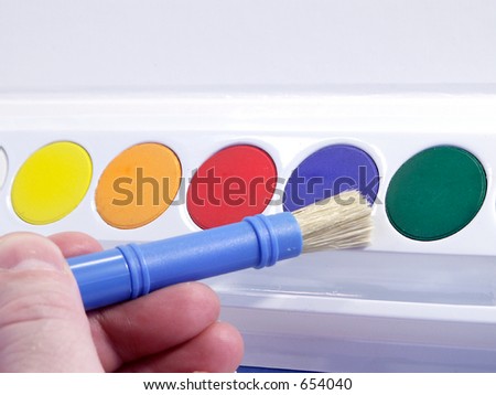 Primary colors in watercolor paint set with brush in hand.