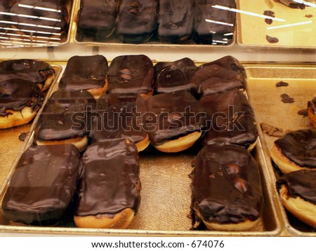 Chocolate covered eclair donuts inside glass case on tray.