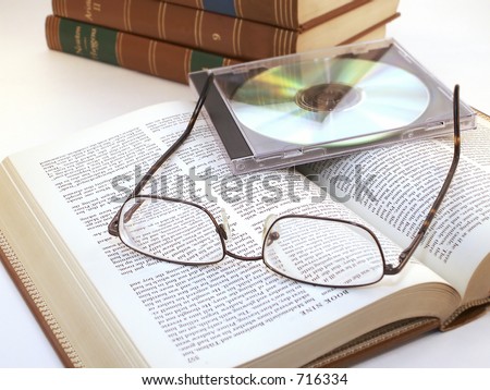 Glasses and CD in case lie on open book with more leather bound books in background.