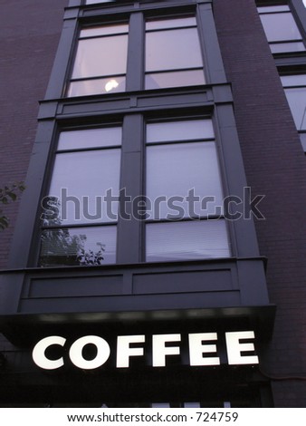Coffee sign lit below large windows of urban loft building in downtown area, late afternoon.