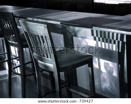 Vintage wooden bar stool casts shadow on bar in this blue-toned black & white shot.