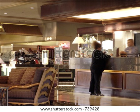 Woman checks in at hotel desk with desk clerk -- coffee bar at back.