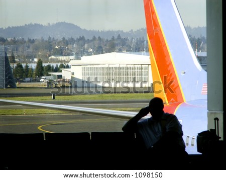 Traveler awaits departure, silhouetted in front of airport window with jet outside.