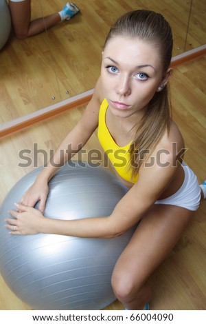 Beautiful blonde girl in shorts sitting with big ball in fitness gym