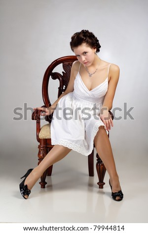 Portrait of beautiful vintage woman in dress sitting on chair on gray background