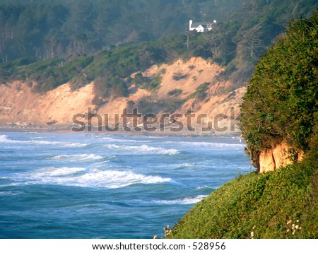 Coastal home on cliff over bright blue sea and waves.