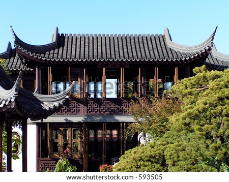 Chinese Pagoda rises over garden on clear day with blue sky at back.